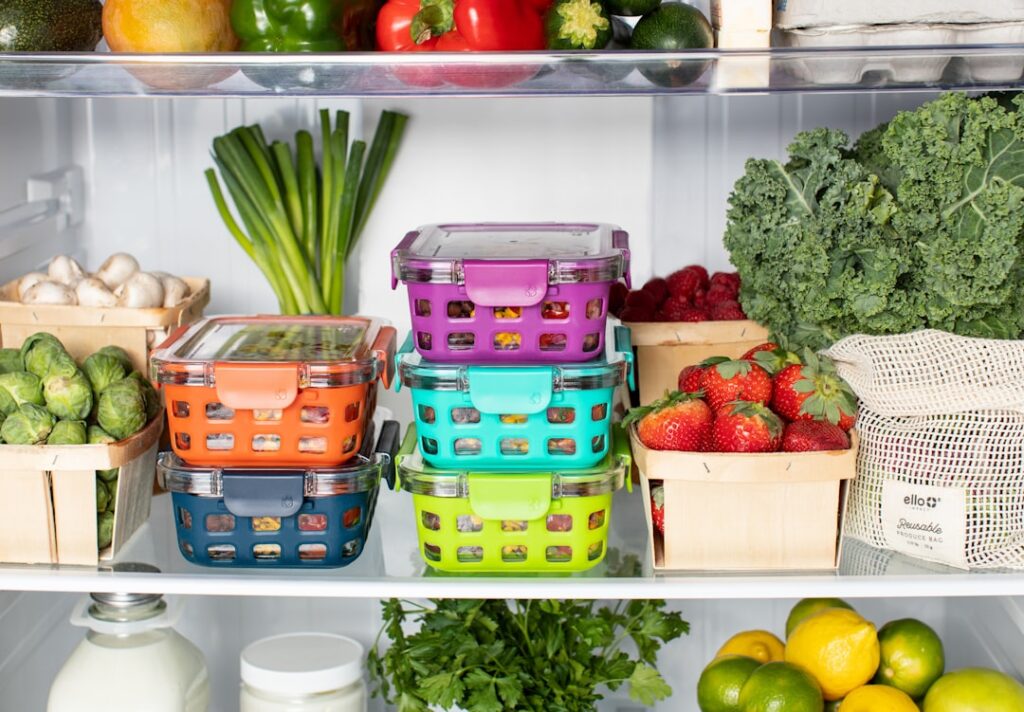 Colorful plastic food containers stacked inside a refrigerator with fresh produce