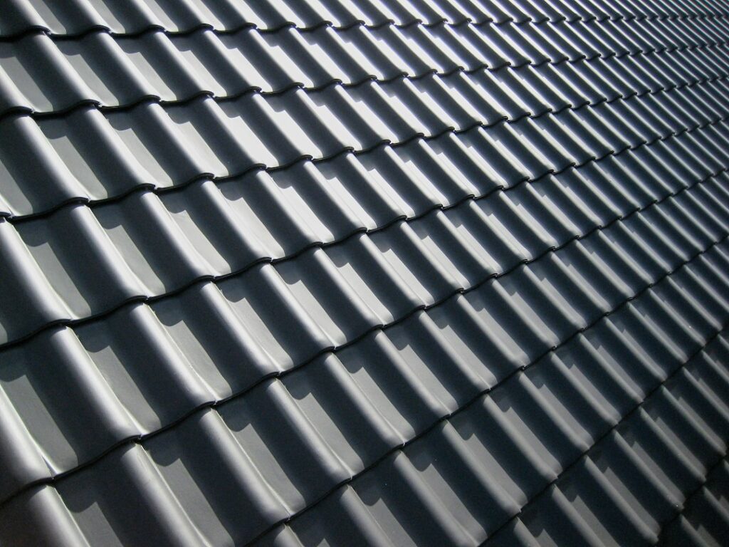 A pattern of dark grey roof tiles with sharp shadows in bright light