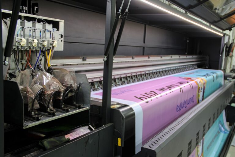 A large industrial printer feeding a long pink banner with printed text