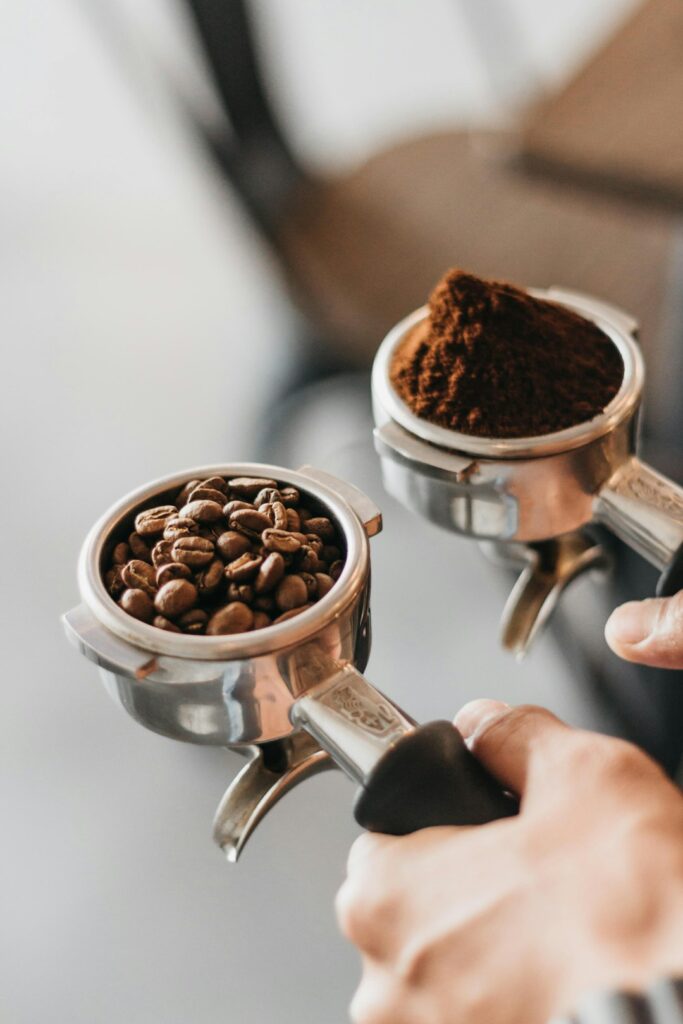 A person holding two portafilters filled with roasted coffee beans and ground coffee