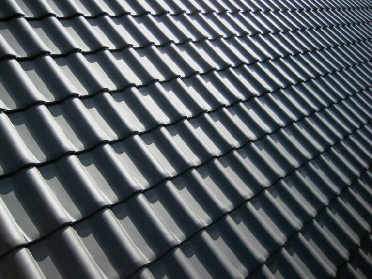 A pattern of dark grey roof tiles with sharp shadows in bright light